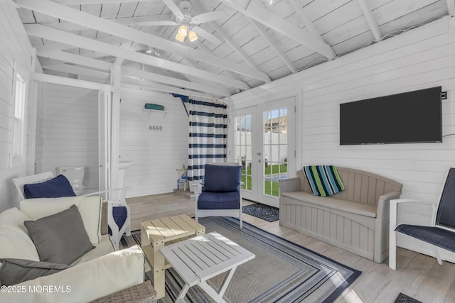 living room with wooden walls, french doors, light hardwood / wood-style floors, and vaulted ceiling with beams