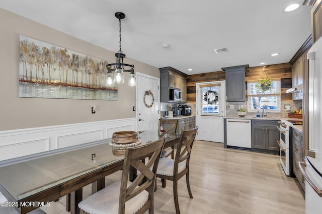 kitchen featuring electric range, sink, backsplash, white dishwasher, and decorative light fixtures