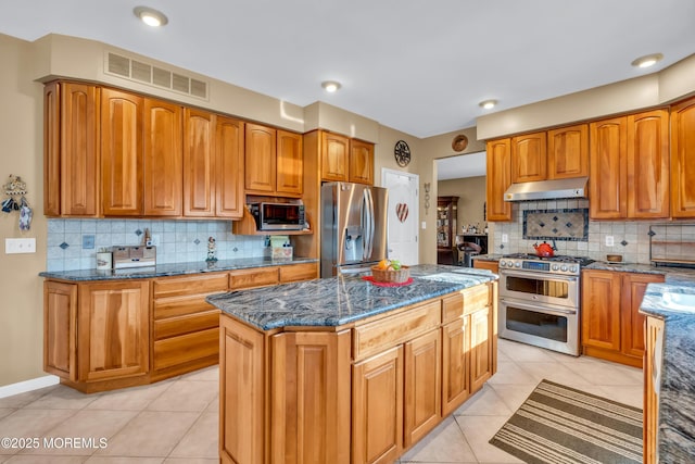 kitchen featuring a center island, stainless steel appliances, dark stone countertops, decorative backsplash, and light tile patterned flooring