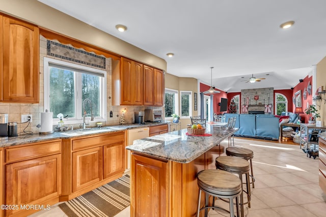 kitchen with sink, ceiling fan, light stone countertops, light tile patterned floors, and a kitchen island