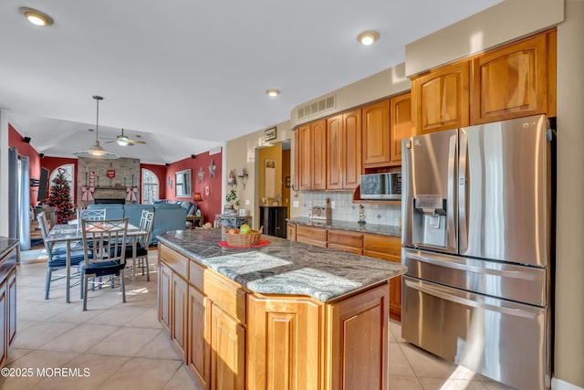 kitchen with dark stone counters, hanging light fixtures, ceiling fan, stainless steel fridge, and a kitchen island