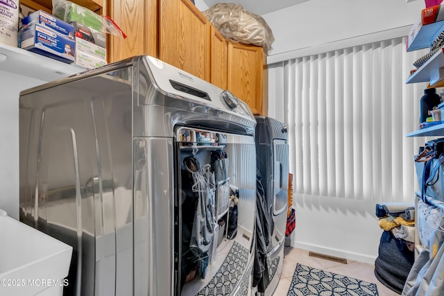 laundry room with washer and dryer, light tile patterned floors, and cabinets