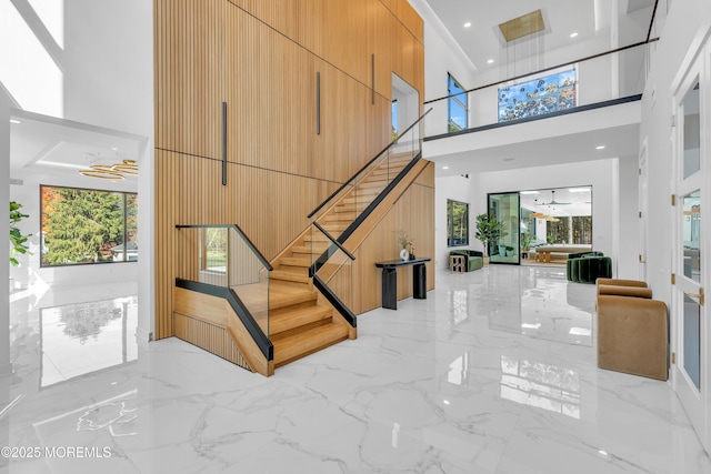 staircase with ceiling fan, wood walls, and a high ceiling