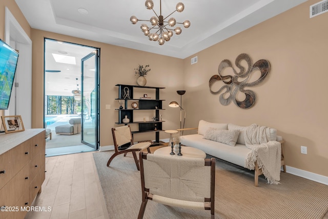 living room featuring a tray ceiling, light hardwood / wood-style flooring, and a notable chandelier