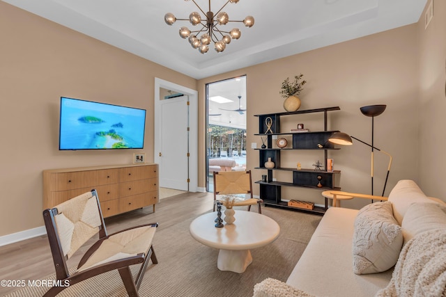 living room featuring a raised ceiling, a chandelier, and light wood-type flooring