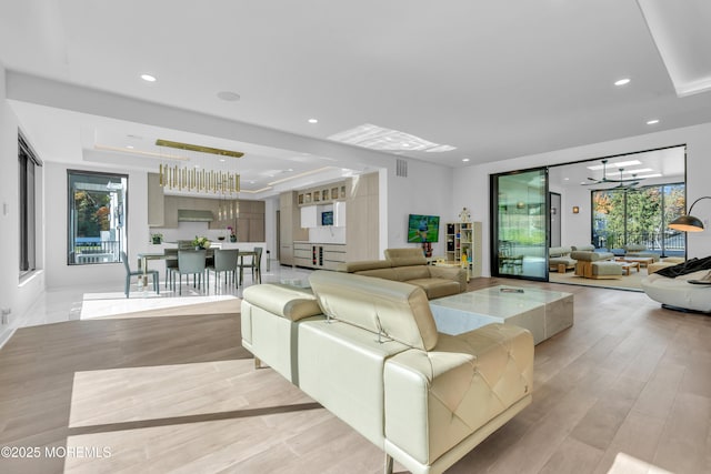 living room featuring light hardwood / wood-style floors, a raised ceiling, and a notable chandelier