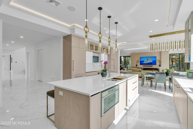 kitchen featuring light brown cabinets, sink, hanging light fixtures, built in microwave, and an island with sink