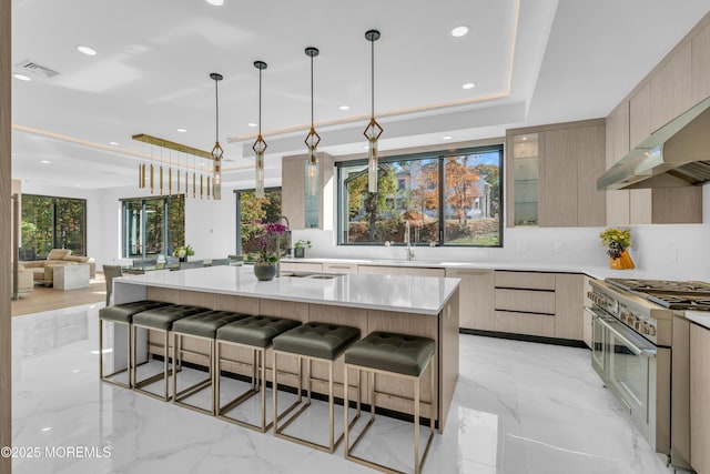 kitchen featuring a breakfast bar, light brown cabinets, a kitchen island with sink, high end stainless steel range oven, and decorative light fixtures