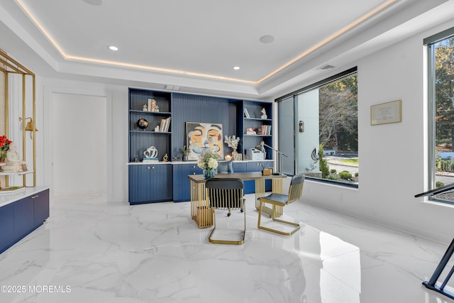 home office with built in shelves, a raised ceiling, and a healthy amount of sunlight