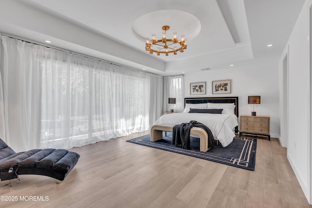 bedroom with light hardwood / wood-style floors, a raised ceiling, and a notable chandelier