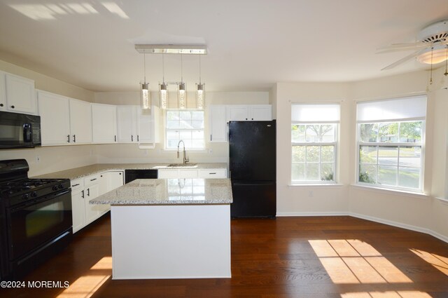 kitchen with pendant lighting, black appliances, sink, a kitchen island, and white cabinetry