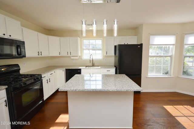 kitchen featuring white cabinetry, light stone countertops, a center island, decorative light fixtures, and black appliances