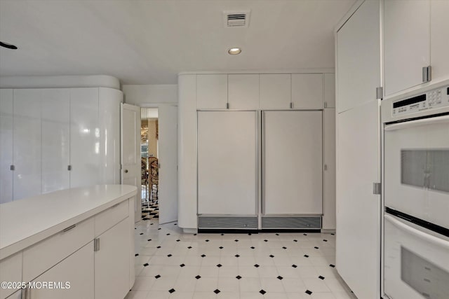 kitchen with paneled fridge, white cabinets, and double oven