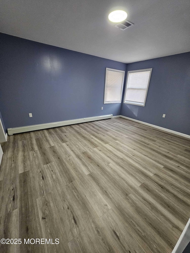 spare room featuring baseboard heating and wood-type flooring