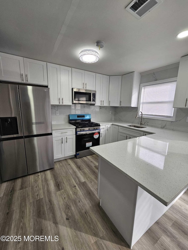 kitchen with hardwood / wood-style floors, white cabinetry, stainless steel appliances, sink, and kitchen peninsula