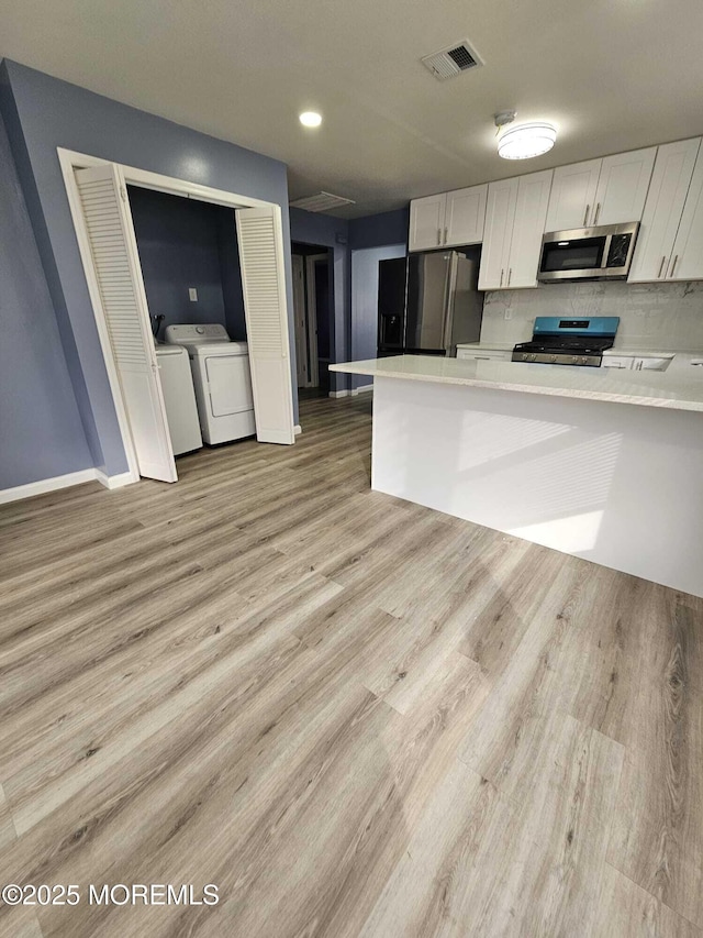 kitchen featuring white cabinetry, light hardwood / wood-style floors, kitchen peninsula, appliances with stainless steel finishes, and washing machine and dryer