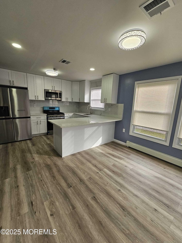 kitchen featuring hardwood / wood-style floors, kitchen peninsula, sink, stainless steel appliances, and white cabinets