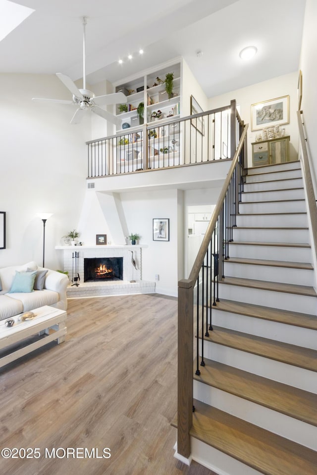 stairs featuring a fireplace, a high ceiling, hardwood / wood-style flooring, and ceiling fan