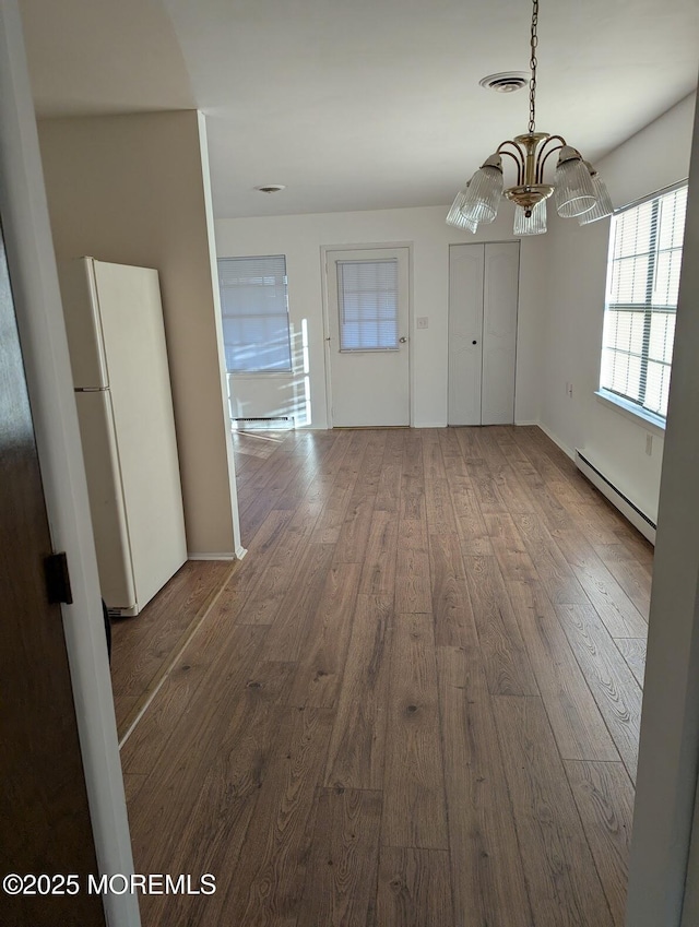 unfurnished dining area featuring baseboard heating, hardwood / wood-style floors, and a chandelier