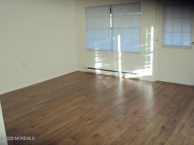 empty room with dark hardwood / wood-style flooring and a baseboard heating unit