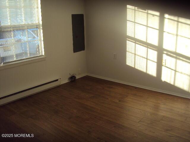 spare room featuring dark hardwood / wood-style flooring, a baseboard radiator, and electric panel