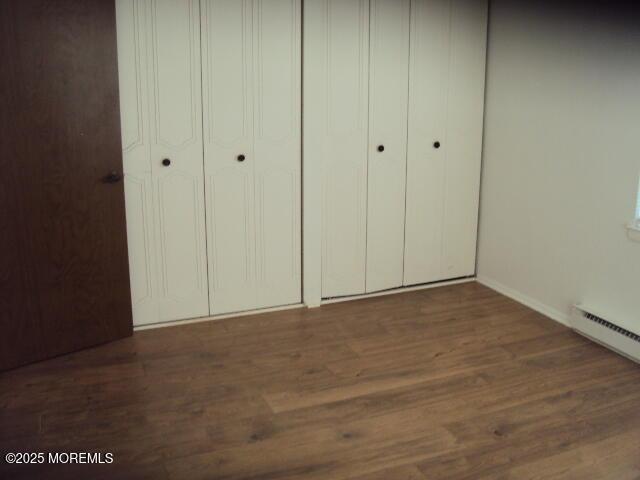 unfurnished bedroom featuring baseboard heating and dark hardwood / wood-style flooring