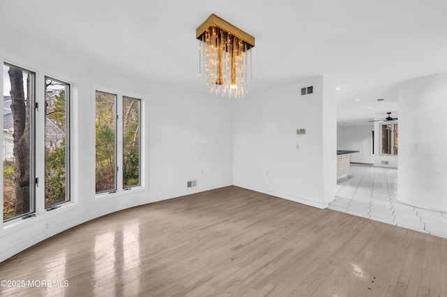 empty room featuring ceiling fan with notable chandelier and light wood-type flooring