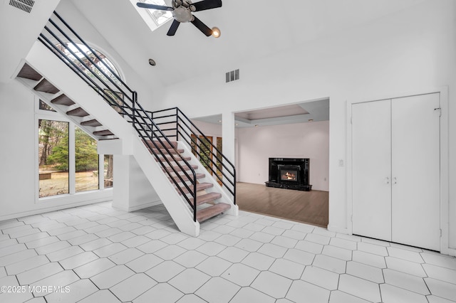 stairway with a skylight, ceiling fan, and high vaulted ceiling