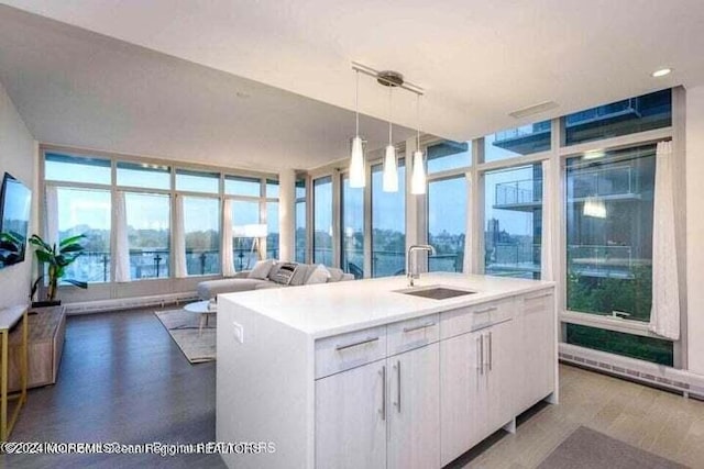 kitchen with decorative light fixtures, white cabinetry, a kitchen island with sink, and sink