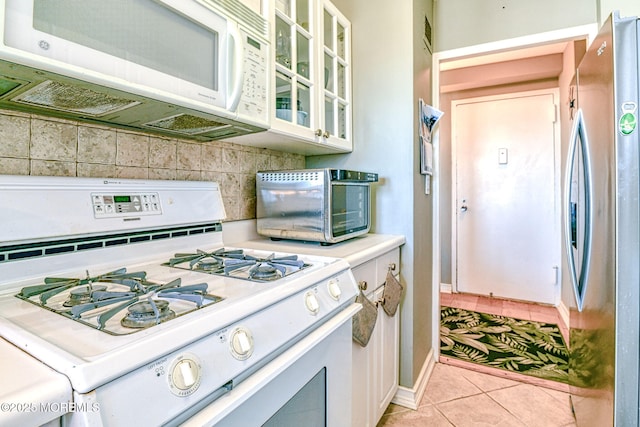 kitchen featuring white appliances, white cabinets, light tile patterned floors, and decorative backsplash