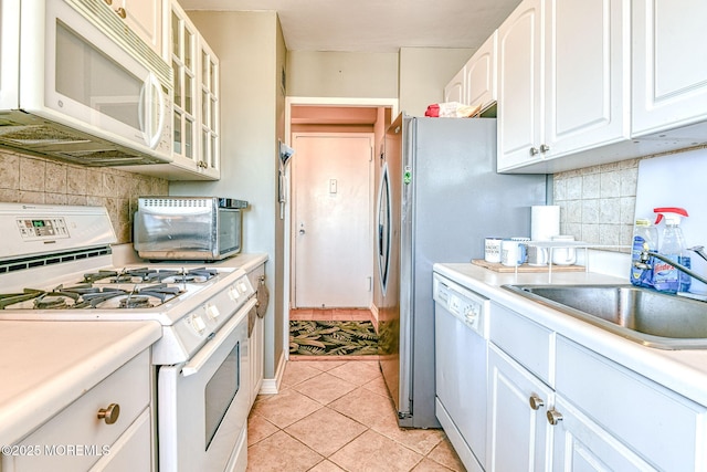 kitchen with white appliances, light tile patterned floors, tasteful backsplash, white cabinets, and sink