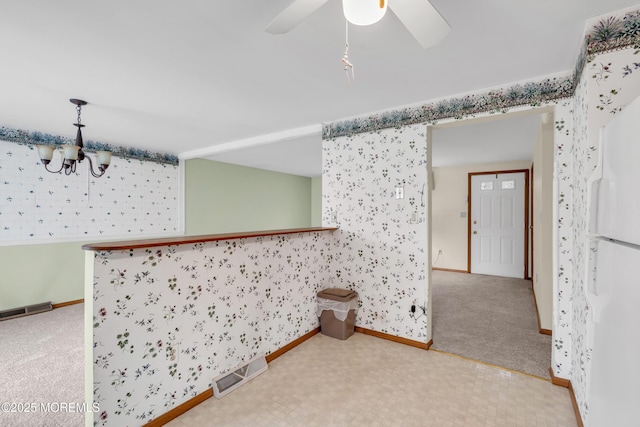 carpeted spare room featuring ceiling fan with notable chandelier