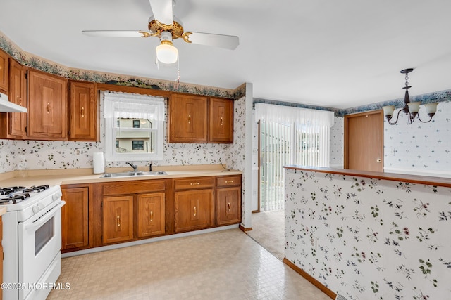 kitchen with white range with gas cooktop, ceiling fan with notable chandelier, hanging light fixtures, and sink