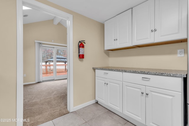 kitchen with light carpet, lofted ceiling with beams, white cabinetry, and light stone counters