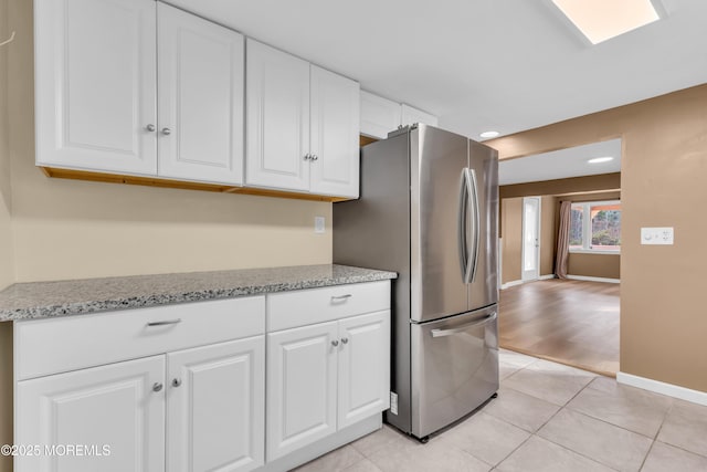 kitchen with stainless steel fridge, light tile patterned floors, white cabinetry, and light stone counters