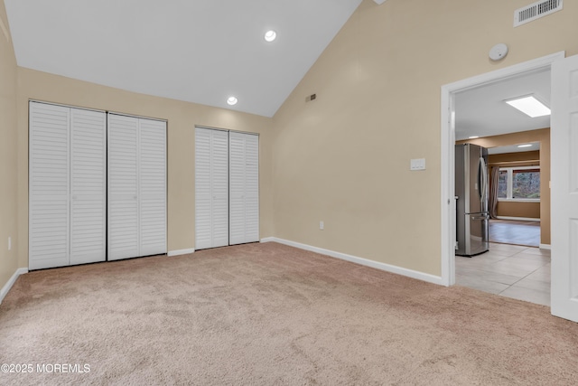 unfurnished bedroom featuring stainless steel fridge, light colored carpet, high vaulted ceiling, and two closets