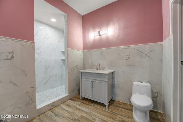 bathroom with a tile shower, vanity, toilet, and tile walls