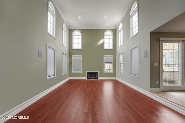 unfurnished living room featuring a towering ceiling, hardwood / wood-style flooring, and crown molding