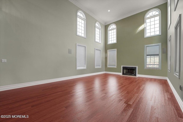 unfurnished living room featuring hardwood / wood-style floors, ornamental molding, and a high ceiling