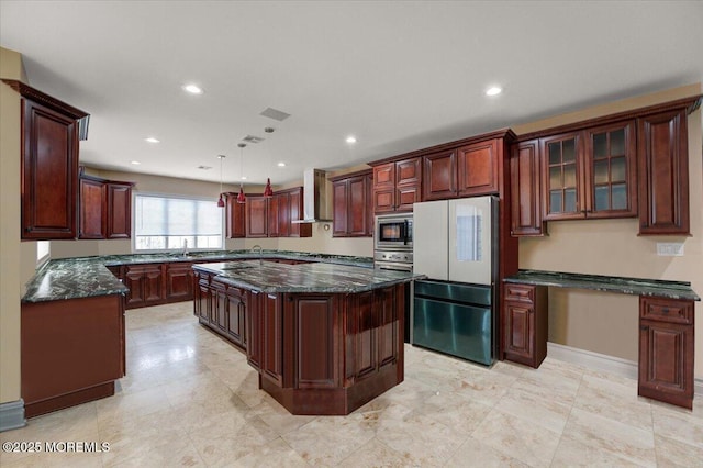 kitchen with appliances with stainless steel finishes, dark stone counters, wall chimney range hood, pendant lighting, and a kitchen island