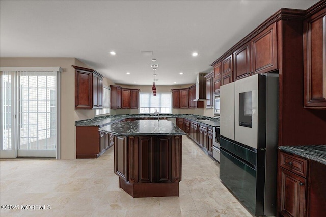 kitchen featuring a center island, hanging light fixtures, stainless steel appliances, wall chimney range hood, and dark stone countertops