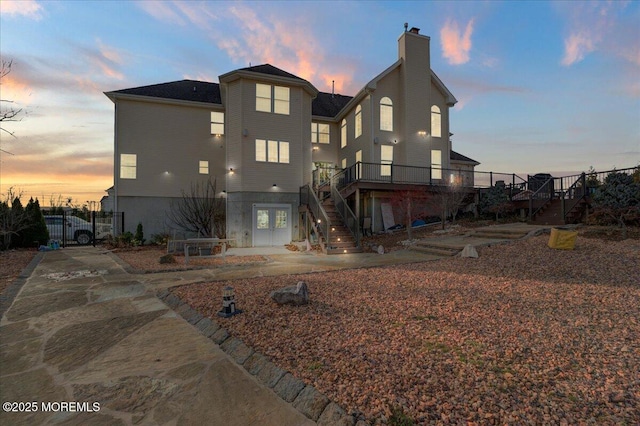 back house at dusk with a wooden deck and french doors