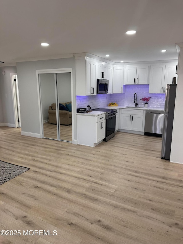 kitchen with white cabinetry, stainless steel appliances, tasteful backsplash, light hardwood / wood-style flooring, and sink