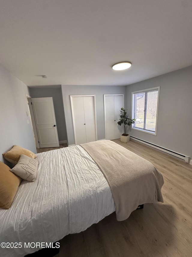 bedroom with a baseboard heating unit, hardwood / wood-style flooring, and two closets