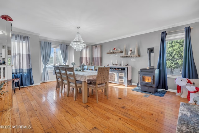 dining space featuring a healthy amount of sunlight, light wood-type flooring, a wood stove, and crown molding