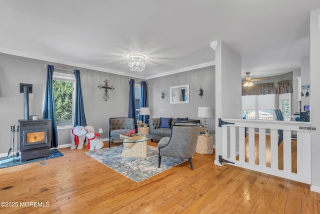 living room with ceiling fan with notable chandelier, light hardwood / wood-style floors, a wood stove, and ornamental molding