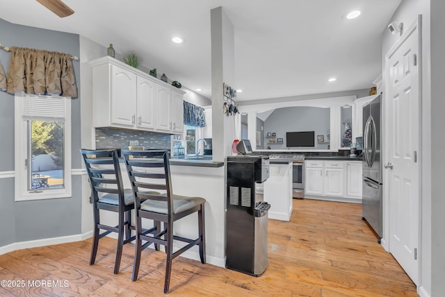 kitchen with kitchen peninsula, decorative backsplash, appliances with stainless steel finishes, light hardwood / wood-style floors, and white cabinetry