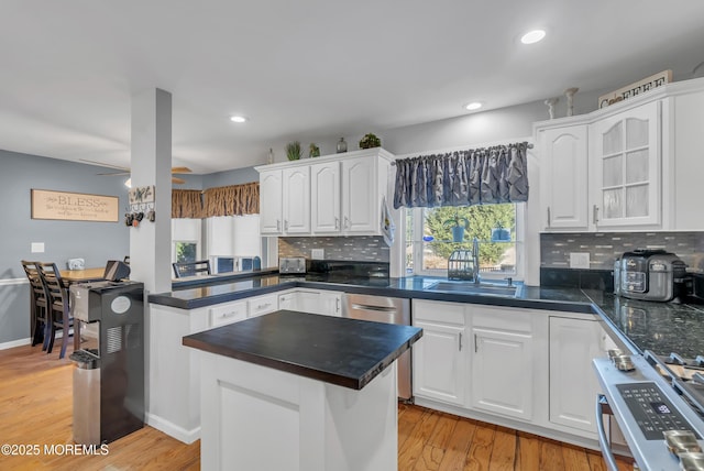 kitchen with light wood-type flooring, backsplash, stainless steel appliances, sink, and white cabinets