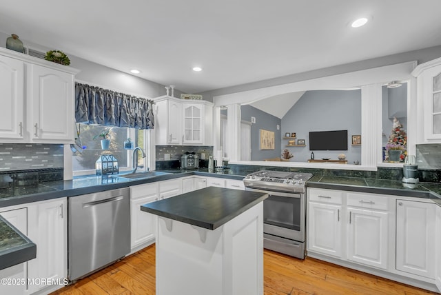 kitchen with decorative backsplash, appliances with stainless steel finishes, a kitchen island, sink, and white cabinetry