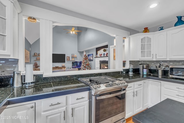 kitchen with backsplash, white cabinets, a stone fireplace, ceiling fan, and stainless steel appliances